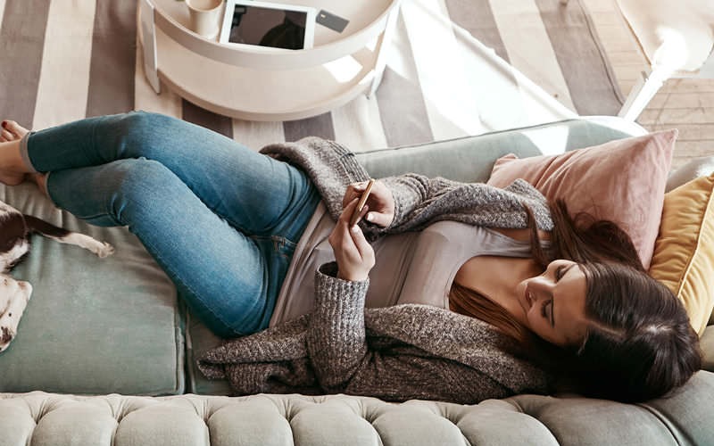 woman relaxing on couch and looks at her cell phone